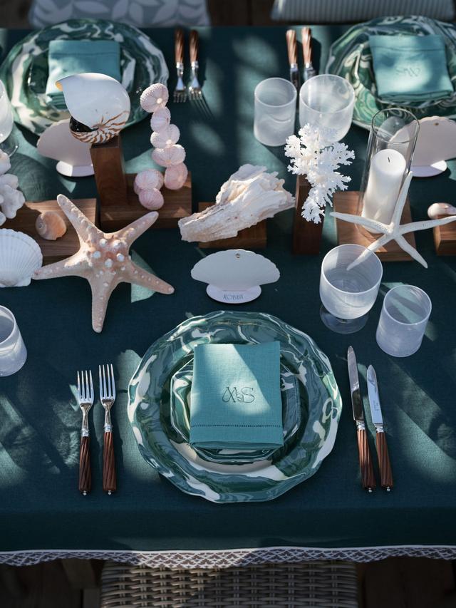 Coastal-inspired wedding tablescape with green linens, patterned plates, seashells and coral details at an Easton Events wedding in St. Tropez.