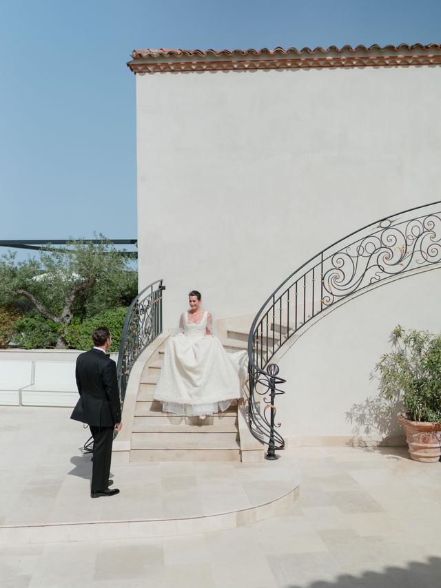 Bride descending a curved staircase to meet the groom during their first look at Château de la Messardière in Saint-Tropez.